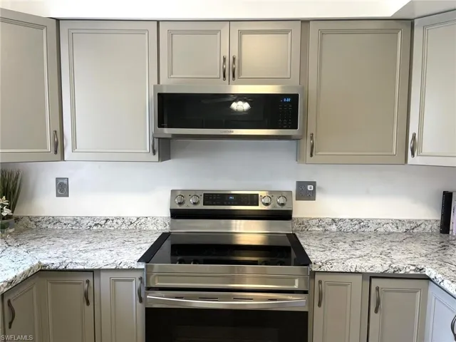 Kitchen with light stone countertops, gray cabinets, and stainless steel appliances