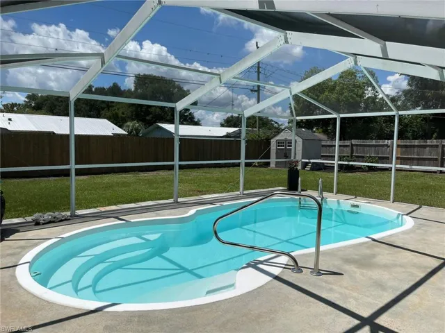 View of pool featuring a storage shed, glass enclosure, a patio area, and a lawn