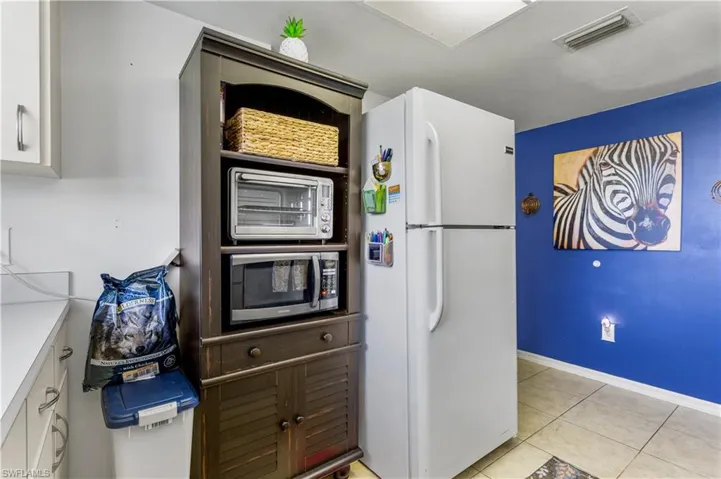 Kitchen with white refrigerator, white cabinets, and light tile patterned flooring