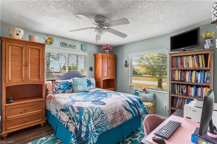 Bedroom with multiple windows, dark hardwood / wood-style flooring, ceiling fan, and a textured ceiling