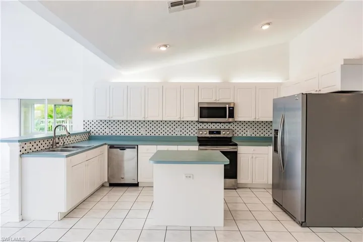 Kitchen with backsplash, sink, appliances with stainless steel finishes, and white cabinetry