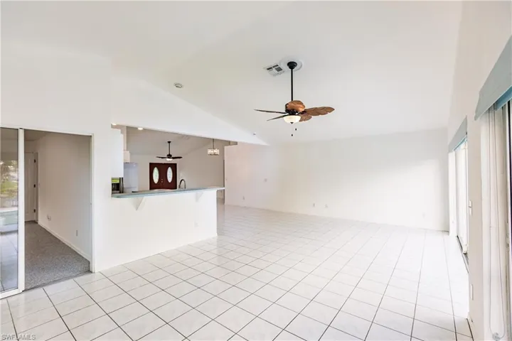 Unfurnished living room featuring ceiling fan, a wealth of natural light, vaulted ceiling, and light tile patterned flooring