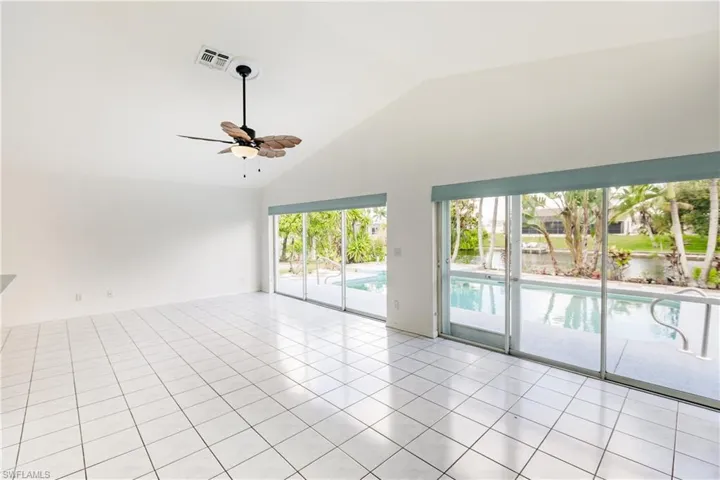 Tiled empty room with plenty of natural light, ceiling fan, and high vaulted ceiling