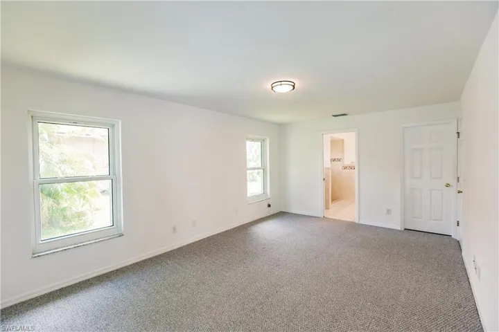 Unfurnished bedroom with light carpet, multiple windows, and ensuite bath