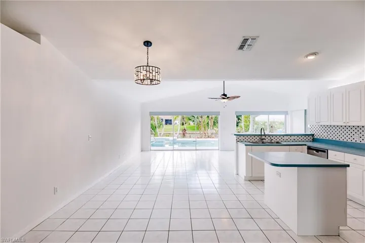 Kitchen featuring white cabinets, light tile patterned floors, vaulted ceiling, sink, and decorative backsplash