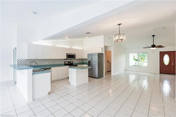 Kitchen with light tile patterned floors, stainless steel appliances, kitchen peninsula, decorative backsplash, and white cabinetry