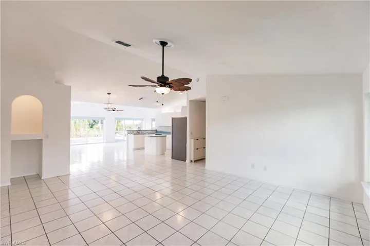 Unfurnished living room featuring lofted ceiling, ceiling fan with notable chandelier, and light tile patterned flooring
