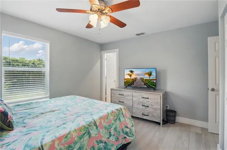Bedroom with light wood finished floors, baseboards, ceiling fan, and visible vents