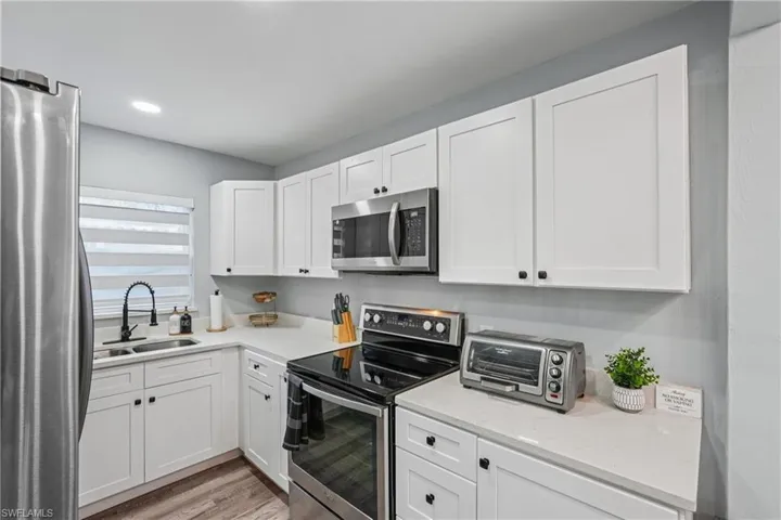 Kitchen featuring appliances with stainless steel finishes, white cabinets, light stone counters, light wood-type flooring, and recessed lighting