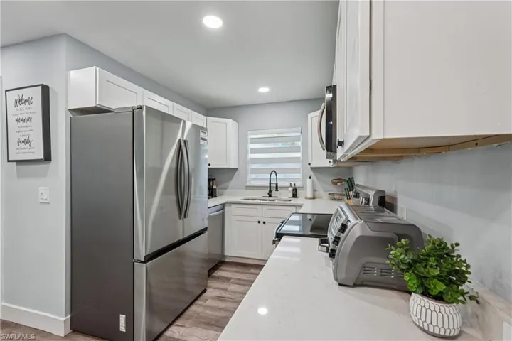 Kitchen featuring appliances with stainless steel finishes, light stone counters, white cabinets, light wood-type flooring, and recessed lighting