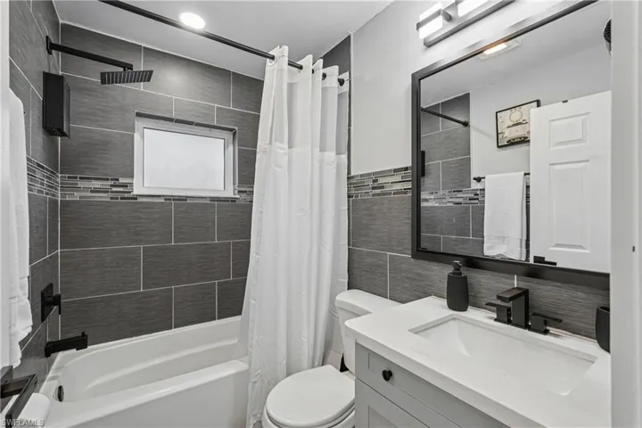 Bathroom with vanity, shower / tub combo, tasteful backsplash, and tile walls