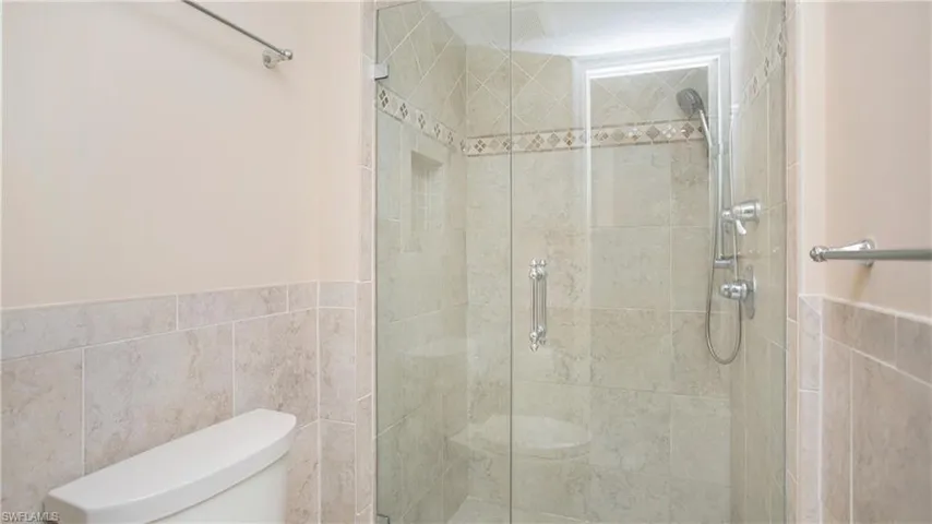 Bathroom with a shower with door, tile walls, and toilet