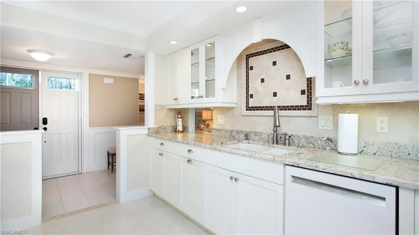 Kitchen featuring white cabinets, dishwasher, light stone countertops, and sink