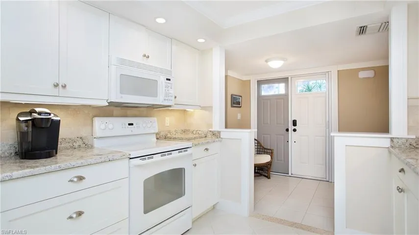 Kitchen featuring light tile patterned floors, white cabinets, white appliances, and ornamental molding