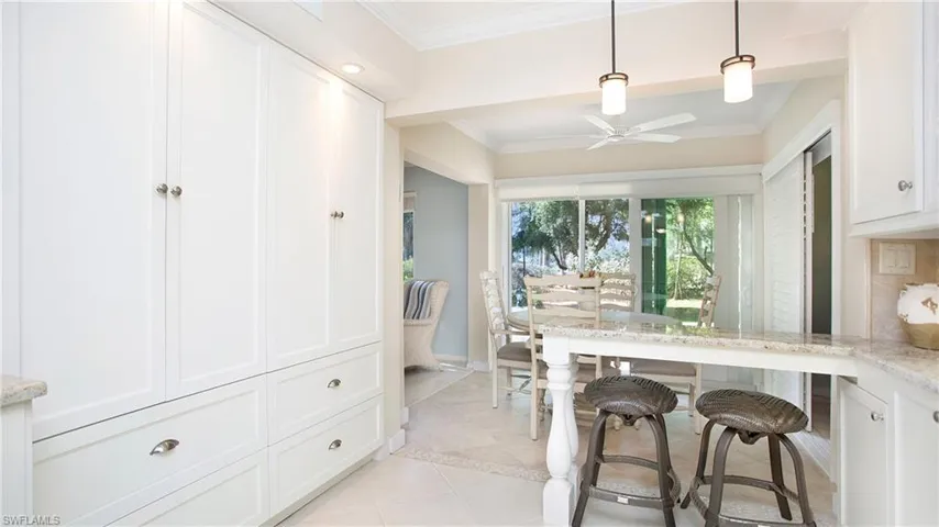 Kitchen with white cabinets, crown molding, light stone counters, and hanging light fixtures