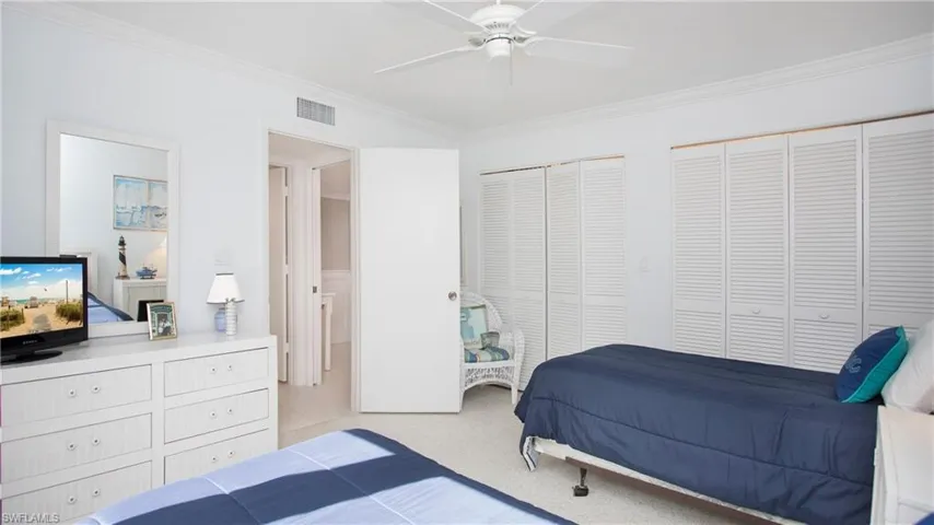 Bedroom with two closets, ceiling fan, ornamental molding, and light colored carpet