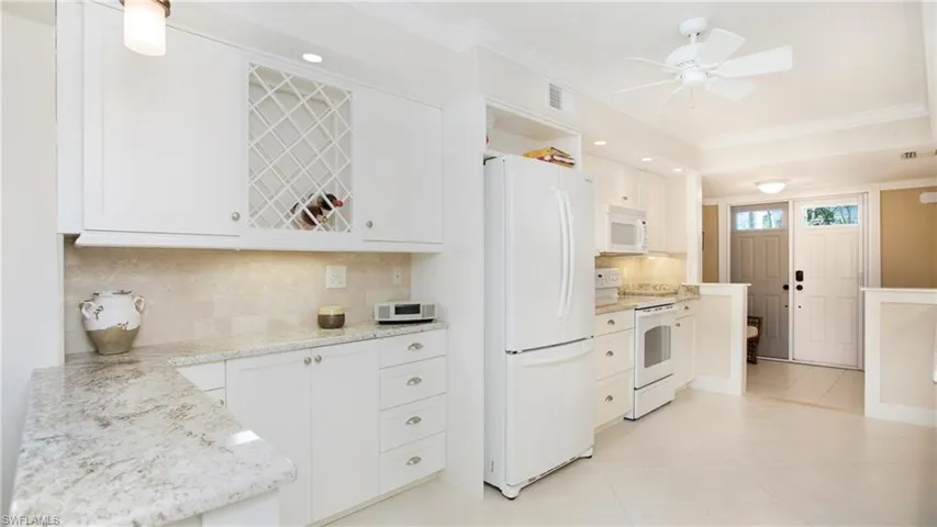 Kitchen with tasteful backsplash, light stone counters, white appliances, white cabinets, and light tile patterned flooring