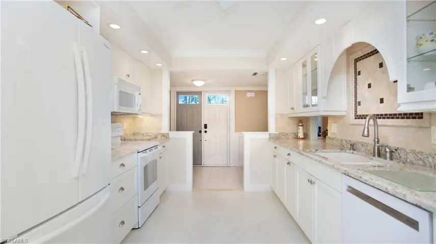 Kitchen with light stone counters, white appliances, crown molding, sink, and white cabinetry