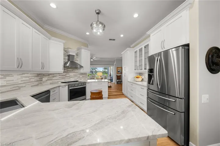 Kitchen featuring appliances with stainless steel finishes, wall chimney exhaust hood, a peninsula, decorative backsplash, and white cabinets