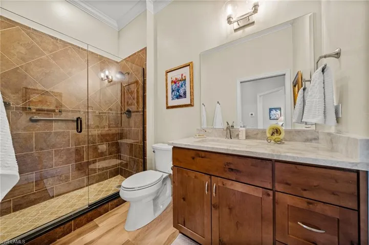 Full bath featuring ornamental molding, toilet, vanity, a stall shower, and wood finished floors