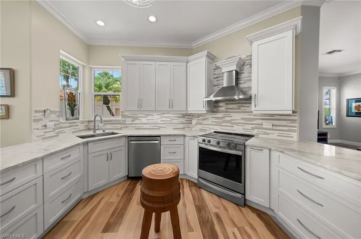 Kitchen featuring stainless steel appliances, a sink, wall chimney range hood, light wood-type flooring, and decorative backsplash