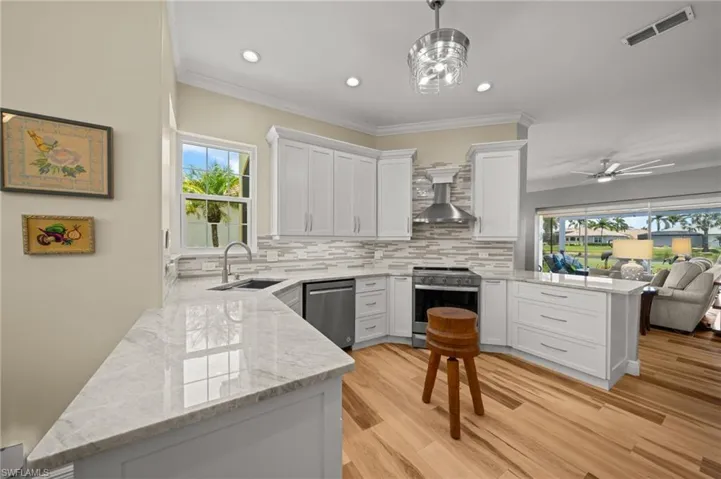 Kitchen with stainless steel appliances, a sink, a peninsula, wall chimney exhaust hood, and backsplash
