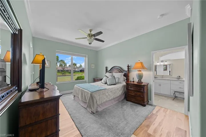 Bedroom featuring light wood-style floors, crown molding, ensuite bathroom, and a ceiling fan