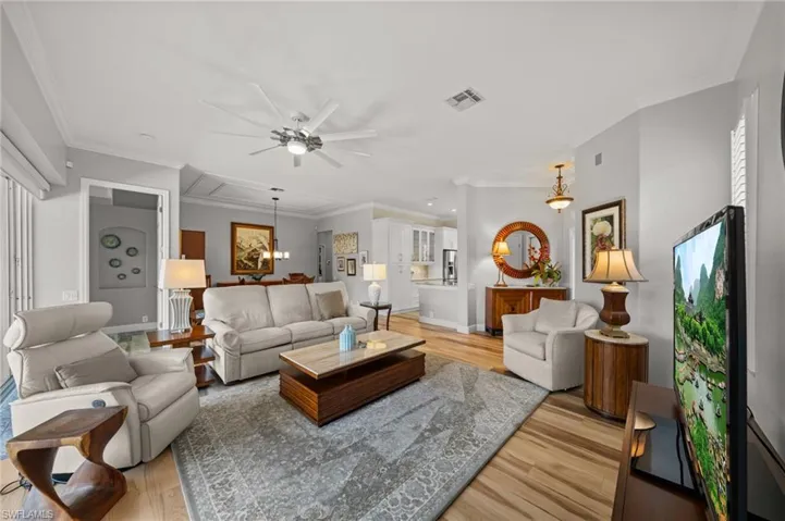 Living room featuring light wood-style floors, ceiling fan, crown molding, attic access, and baseboards