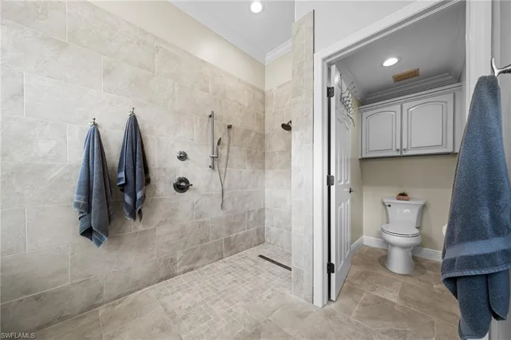 Bathroom featuring tiled shower, ornamental molding, toilet, recessed lighting, and baseboards