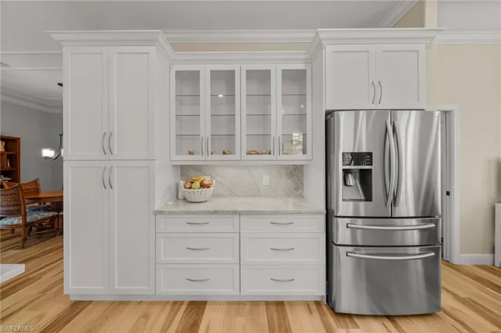 Kitchen with stainless steel refrigerator with ice dispenser, white cabinetry, crown molding, glass insert cabinets, and light stone counters