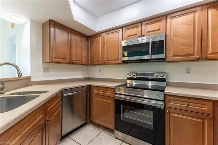 Kitchen with stainless steel appliances, brown cabinetry, light tile patterned floors, and light stone counters