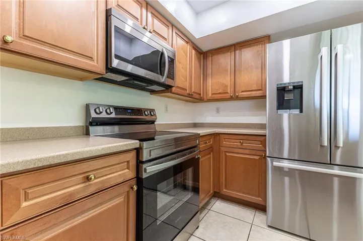 Kitchen featuring stainless steel appliances, light tile patterned floors, brown cabinets, and light stone countertops