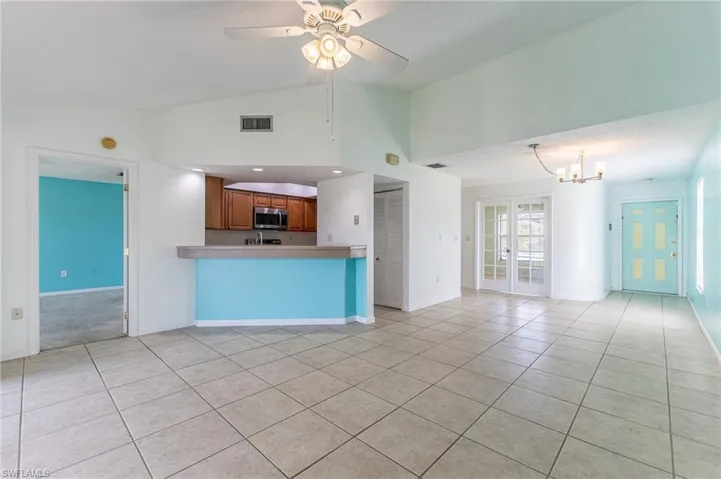 Kitchen featuring light tile patterned floors, brown cabinets, open floor plan, stainless steel microwave, and high vaulted ceiling