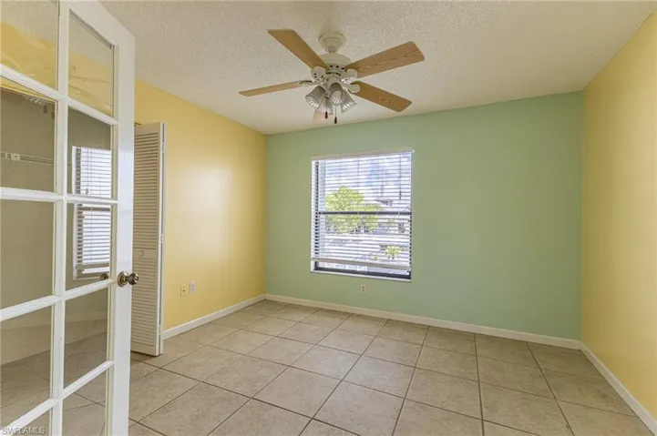 Empty room with a textured ceiling, light tile patterned floors, and ceiling fan