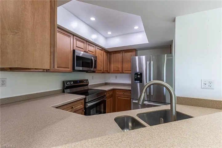Kitchen featuring appliances with stainless steel finishes, recessed lighting, brown cabinets, and light stone counters