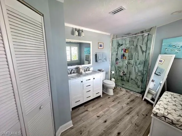 Primary Bathroom with a closet, double vanity, a marble finish shower, light wood-style floors, and ornamental molding