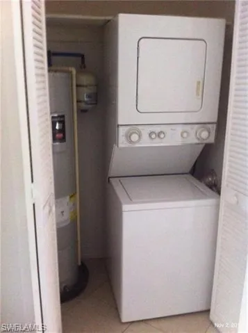 Washroom featuring stacked washer and clothes dryer, light tile patterned floors, and electric water heater