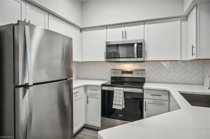 Kitchen with stainless steel appliances, hardwood / wood-style floors, backsplash, and white cabinetry