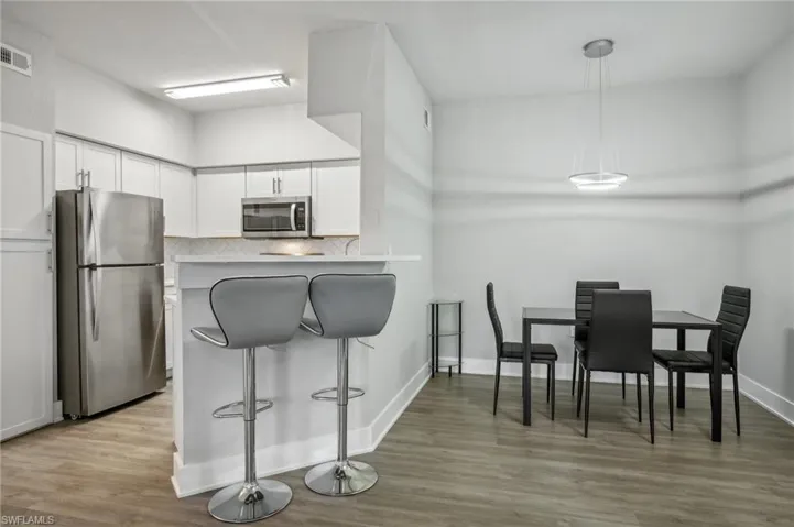 Kitchen featuring light hardwood / wood-style floors, stainless steel appliances, tasteful backsplash, white cabinetry, and pendant lighting