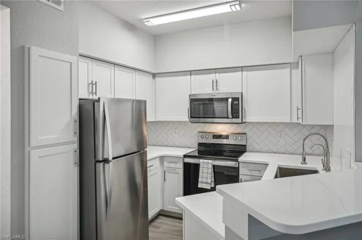 Kitchen with light wood-type flooring, appliances with stainless steel finishes, white cabinets, kitchen peninsula, and sink