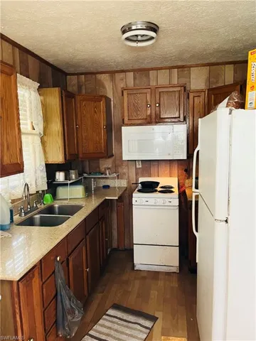 Kitchen with dark hardwood / wood-style flooring, wood walls, sink, white appliances, and a textured ceiling