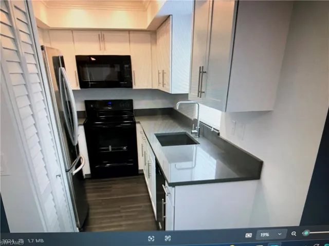 Kitchen with black appliances, dark wood-style floors, white cabinets, and ornamental molding
