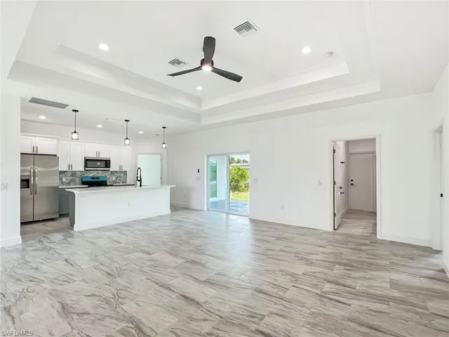Unfurnished living room featuring ceiling fan, sink, light tile flooring, and a raised ceiling