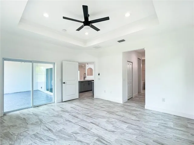 Unfurnished bedroom featuring access to exterior, ensuite bathroom, ceiling fan, and a raised ceiling