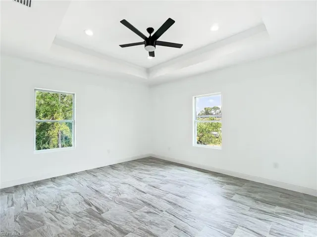 Tiled spare room featuring a healthy amount of sunlight, ceiling fan, and a tray ceiling