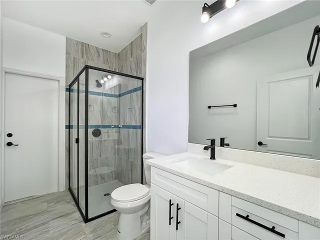 Bathroom with a shower with shower door, vanity with extensive cabinet space, tile flooring, and toilet