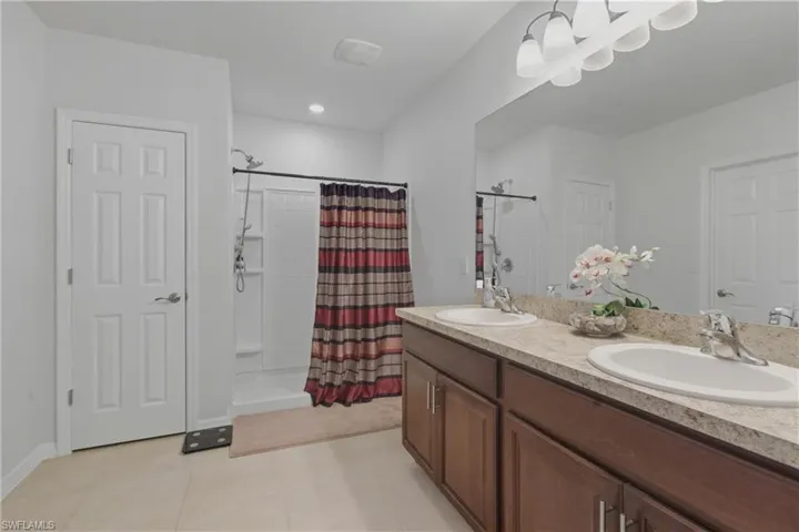 Bathroom featuring double vanity, light tile patterned flooring, and a shower stall