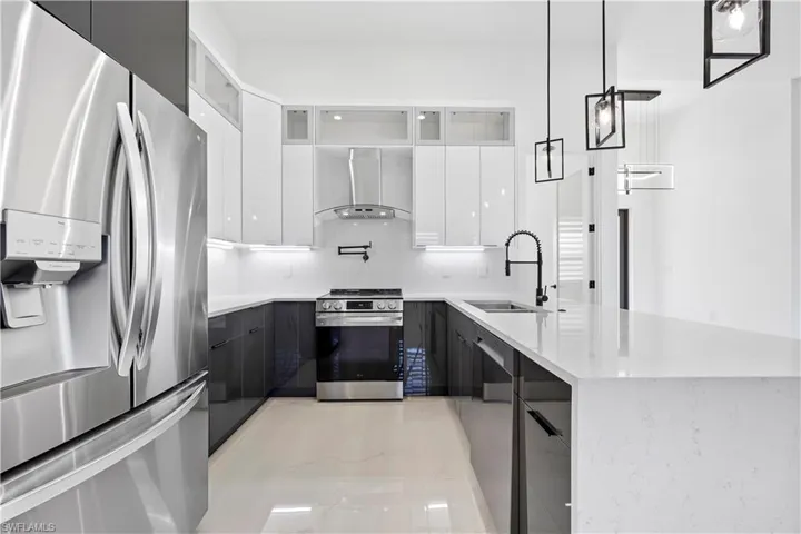 Kitchen with wall chimney exhaust hood, modern cabinets, appliances with stainless steel finishes, and a sink