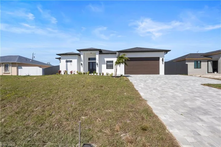Prairie-style home with decorative driveway, a front lawn, an attached garage, and fence