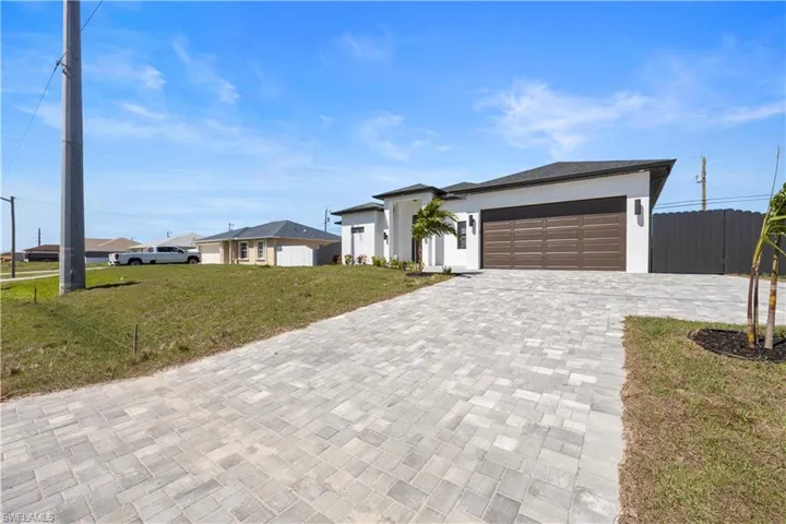 View of front facade with a front lawn, fence, stucco siding, decorative driveway, and an attached garage